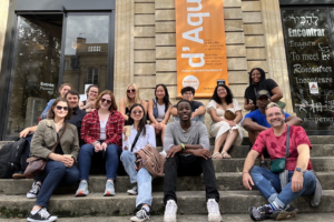 A group of Davidson in France participants and faculty director seated on stairs outside a building