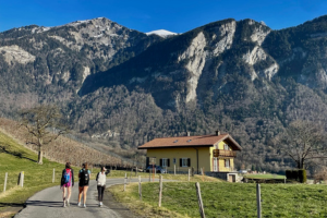 Three students walking on a path in front of snow-covered mountains